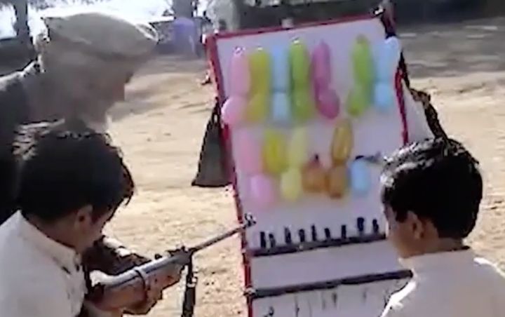 A man instructs two boys on shooting balloons with a BB gun 