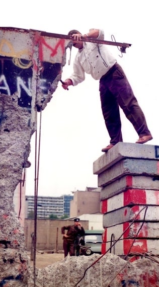 <em>Unidentified man hacks away at the Berlin Wall while East German Guard looks on.</em>
