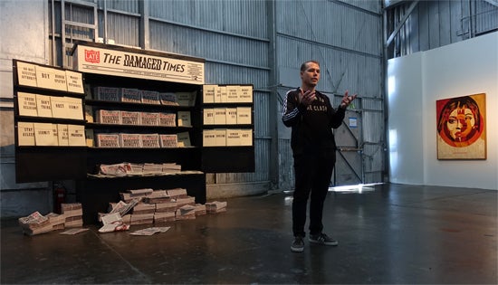 Shepard Fairey in front of The Damaged Times Newsstand installation; Background artwork - Media Target