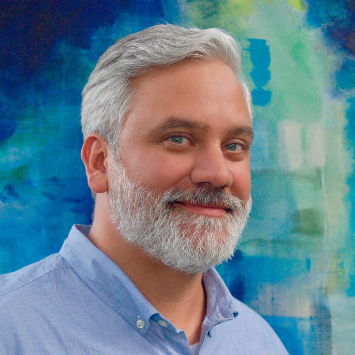 <p>Roger Hutchison stands in front of a painting from<em> My Favorite Color is Blue. Sometimes.</em></p>