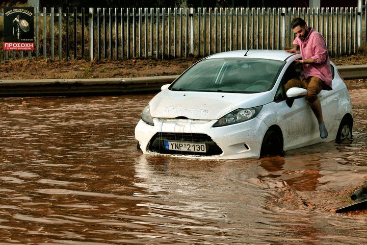 A man tries to get into a car stuck in floodwater in the town of Mandra.