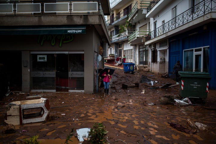 A woman with an umbrella stands in a flooded street next to a damaged shop.