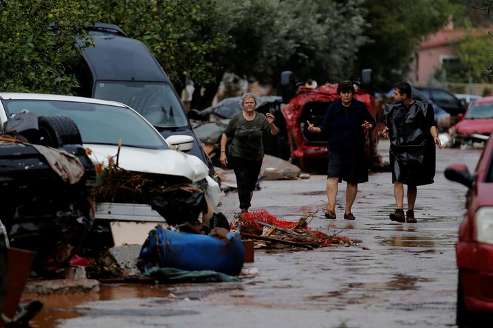 Locals walk next to destroyed cars following heavy rainfall.