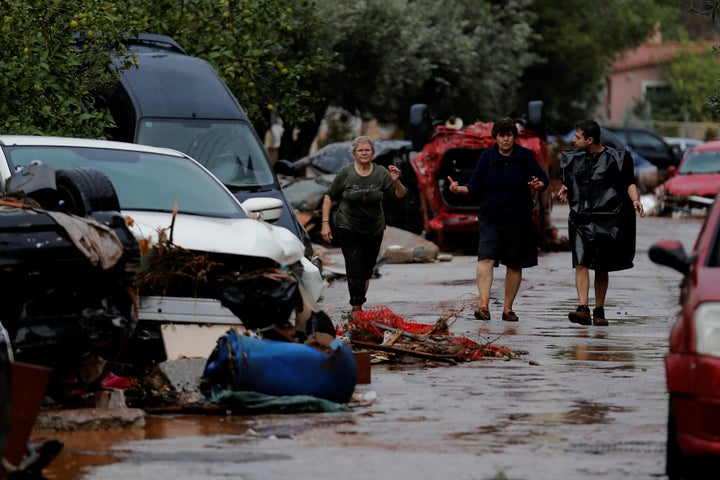 Locals walk next to destroyed cars following heavy rainfall.