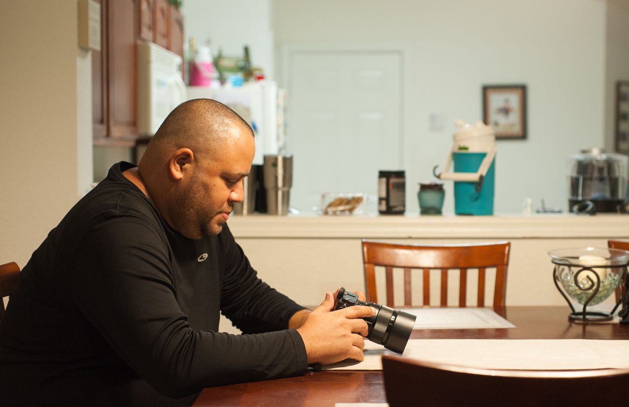 Delgado, in his home, looks at his camera. He took up photography after the Pulse shooting as a way to cope with his PTSD.