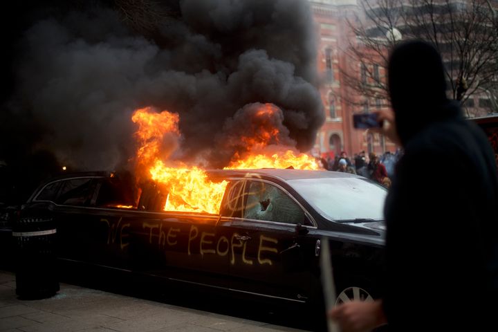 A limousine with the graffiti of "We the People" spray-painted on the side is set ablaze.