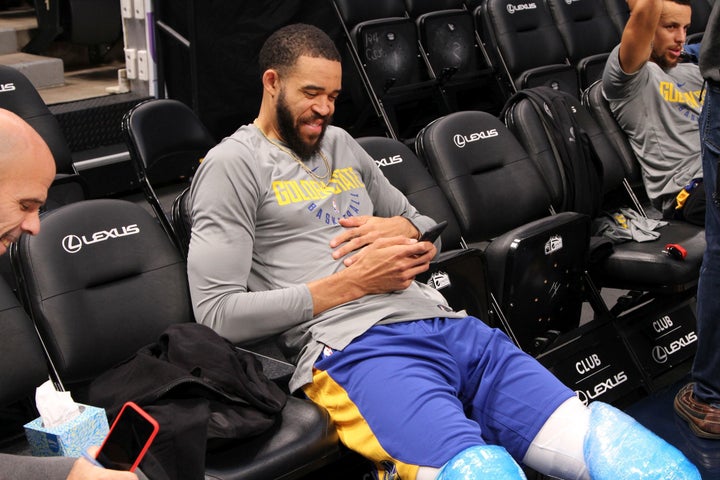 Golden State Warriors center JaVale McGee laughs with Vice President of Communications Raymond Ridder while Stephen Curry answers media questions in the background.