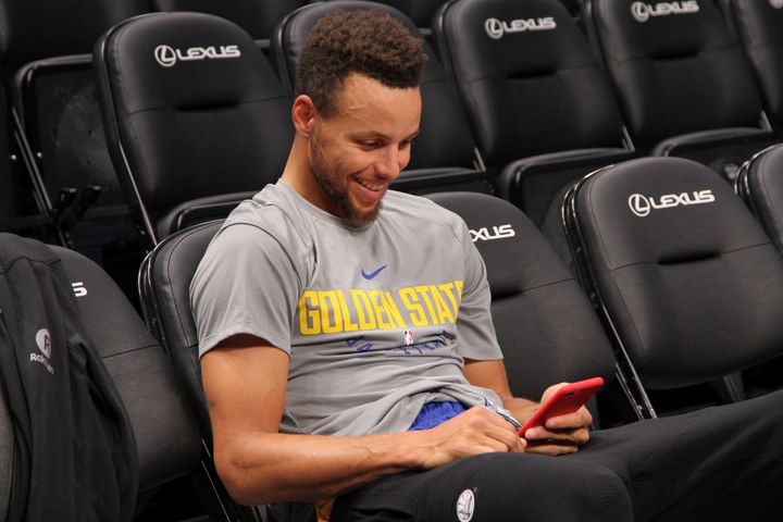 Stephen Curry laughs while looking at his phone following morning shoot around.