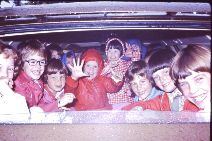 Heidi sits center, in the red hooded coat. Her little sister is next to her, wearing the gingham coat. Her older sister is second from the far right.