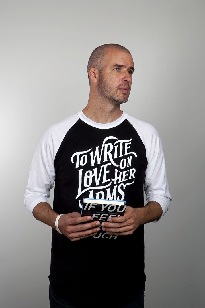 Jamie Tworkowski wearing a TWLOHA shirt and holding a copy of his book, ‘If You Feel Too Much.’