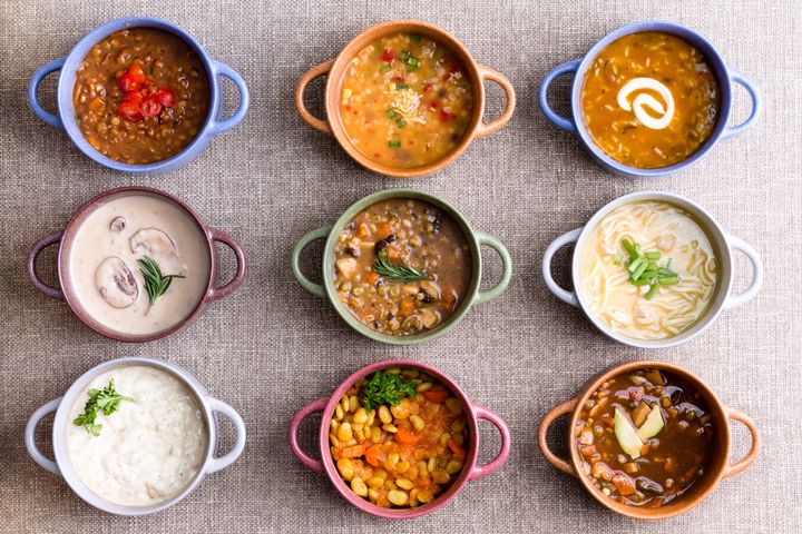 Assorted soups from worldwide cuisines displayed in bowls in three colorful lines garnished with cream and herbs in a World Of Soup concept, overhead view Ozgur Coskun via Getty Images