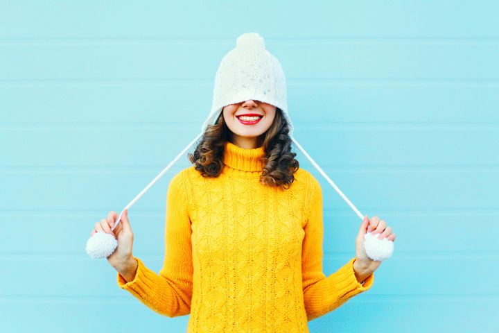 Fashion happy young woman in knitted hat and sweater having fun over colorful blue background Rohappy via Getty Images