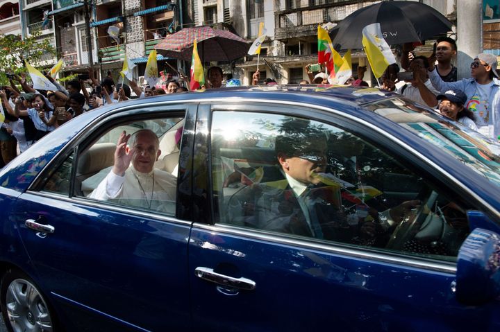 Pope Francis waves to well-wishers as he is driven through the streets of downtown Yangon on November 27, 2017. Pope Francis arrived in mainly Buddhist Myanmar on November 27 where he was set to meet army chief Min Aung Hlaing, the man accused of overseeing a brutal campaign to drive out the country's Rohingya Muslim minority.