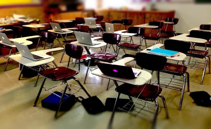 <p>Alt Text: Photograph of a classroom with individual desks. Many desks have open laptops on them. </p>