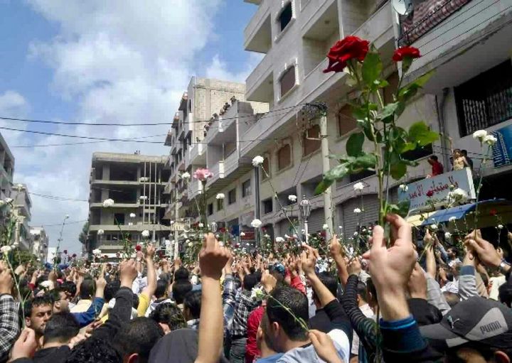 Protestors march with flowers and offer water and roses to armed Syrian soldiers 