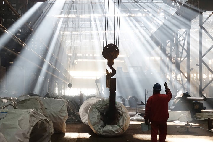 A worker watches as steel wire rolls are hoisted up at a plant in Dalian, China. 