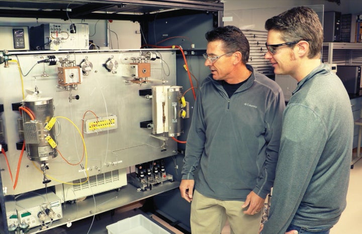 Troy Semelsberger (left) and Andrew Sutton stand alongside the continuous flow reactor developed by their team. This high-throughput environment stands to improve biofuels production by enabling more efficient chemical conversion of biomass into hydrocarbon fuels.