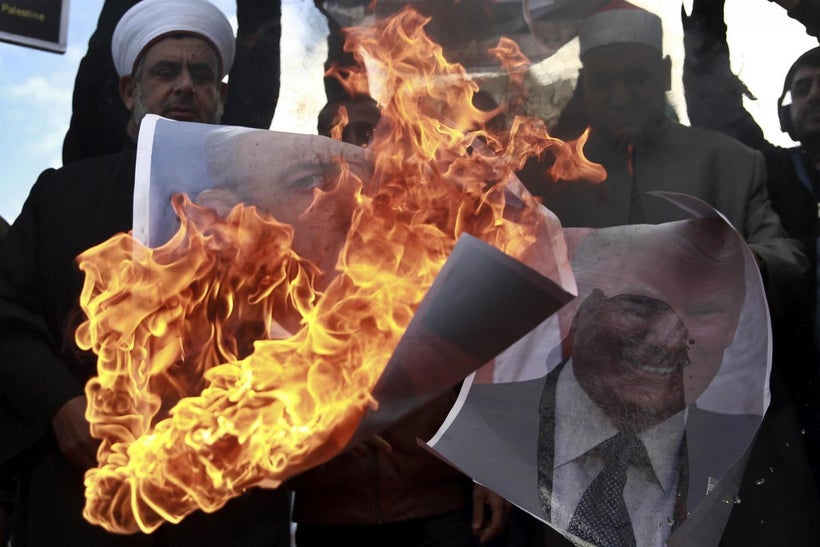 Palestinians burn posters of Israeli Prime Minister Benjamin Netanyahu and U.S. President Donald Trump, during a protest aga