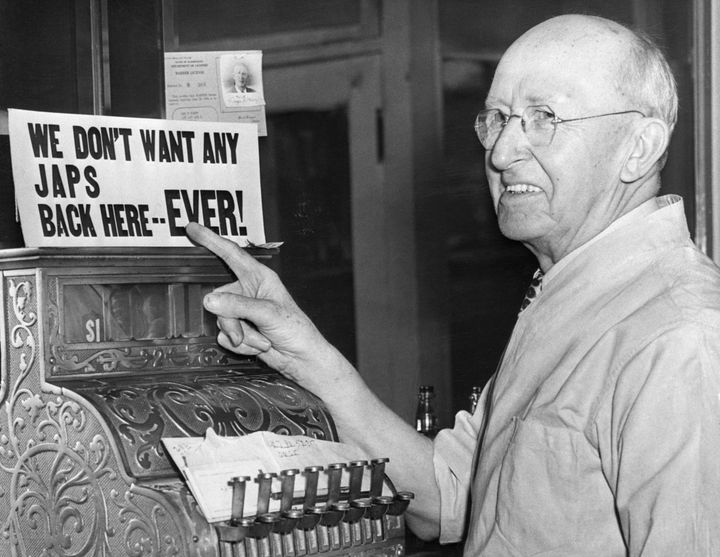 A barber points to his own anti-Japanese sign after Japanese-Americans were incarcerated during World War II.