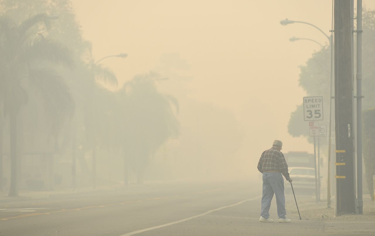 A man walks along a road as the Thomas fire leaves smoke in Ventura.