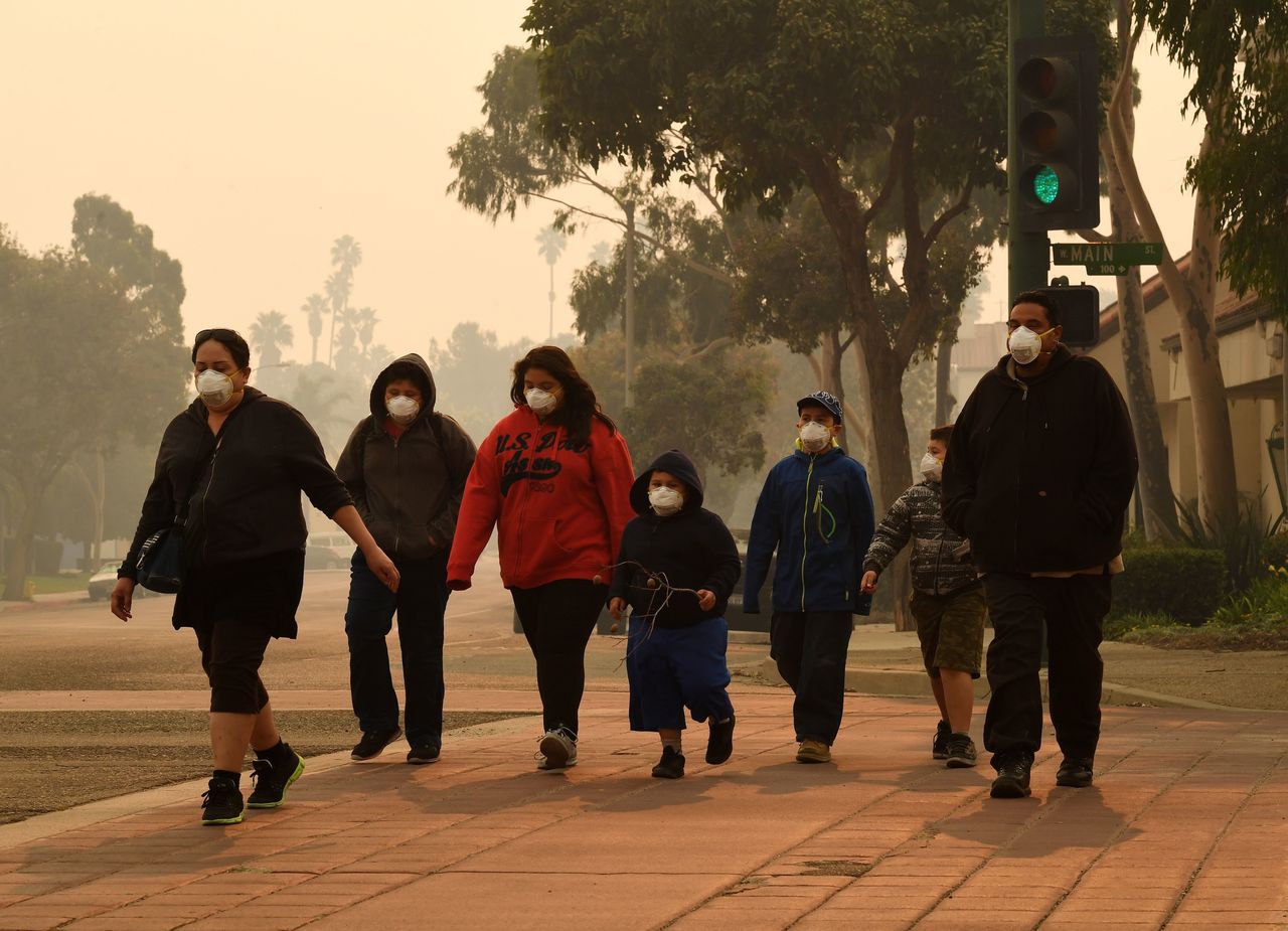 A family wears masks as they walk through the smoke-filled streets after the Thomas fire swept through Ventura County.
