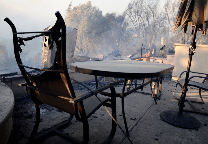 Burnt chairs in front of a swimming pool beside a house destroyed by fire.