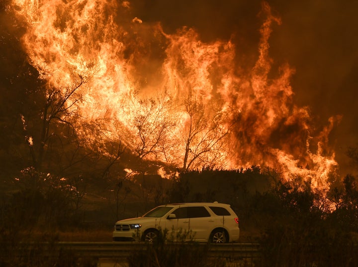 Vehicles pass beside a wall of flames on the 101 highway near Ventura, California, on Dec. 6, 2017. 