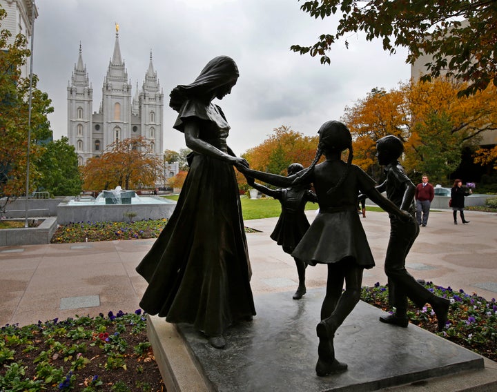 A statue of a mother and her children on the main campus of the World Headquarters of the Church of Jesus Christ of Latter-Day Saints, with the Mormon Salt Lake Temple in the background.