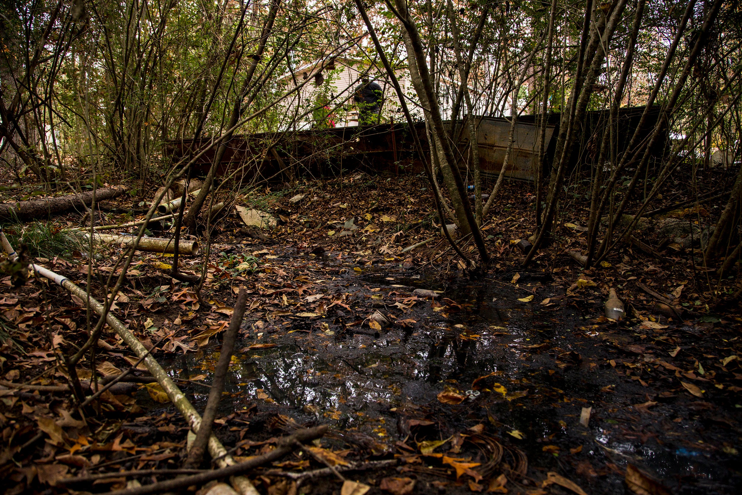 Two PVC pipes empty raw waste into a wooded area near a group of trailers. A slimmer pipe zigzags across the sewage and carri
