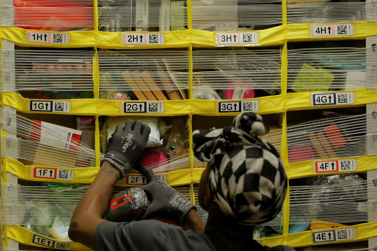 A worker sorts products into bins inside of a large Amazon fulfillment center.