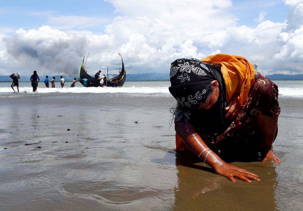 An exhausted Rohingya refugee woman touches the shore after crossing the Bangladesh-Myanmar border by boat through the Bay of