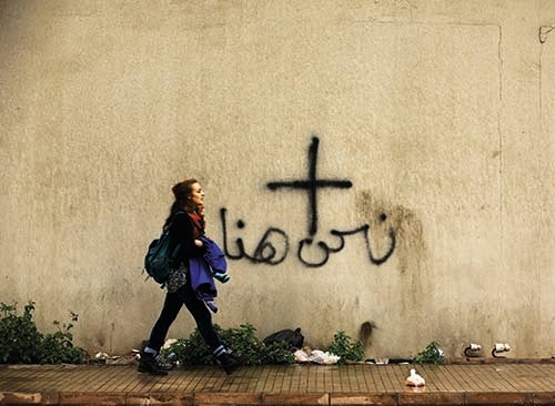 A woman walks past graffiti depicting a cross and the words “we are here” in a Christian-dominated eastern suburb of Beirut (courtesy AFP)