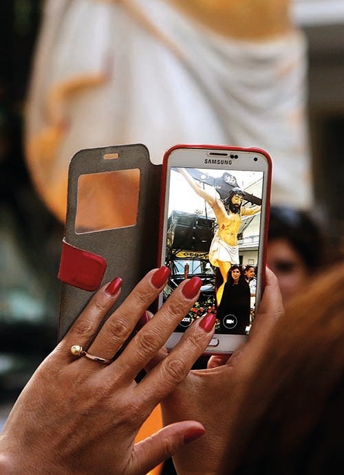 A woman shoots a picture of her friend posing under a crucifix on a vehicle during a Greek Orthodox procession marking Good Friday in Beirut (courtesy AFP)