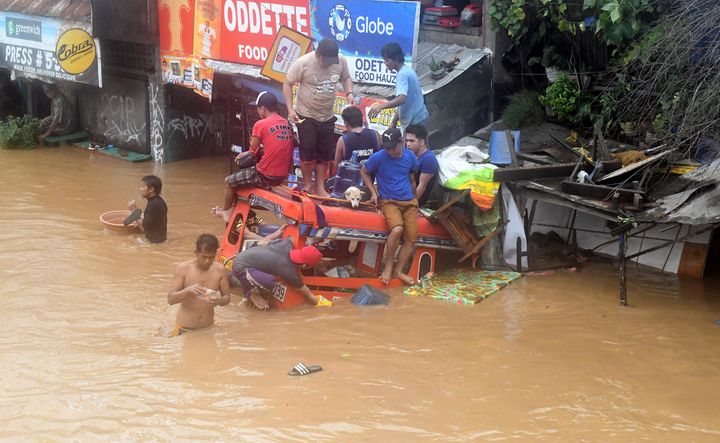 Residents are seen on the top of a partially submerged vehicle along a flooded road in Cagayan de Oro city in the Philippines on Dec. 22.