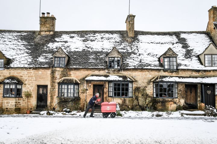A postman pushes his trolley past snow-covered cottages on the High Street in Broadway, Worcestershire 