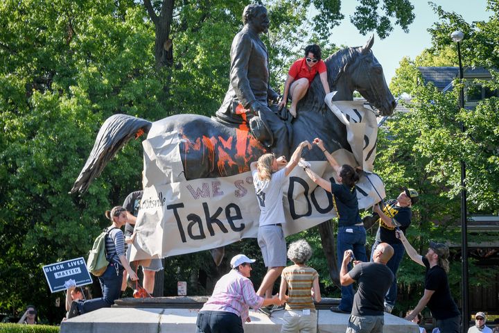 Members of a racial justice organization prepare to hang a banner that says, "Louisville, take it down" on a Confederate monument on Aug. 19.