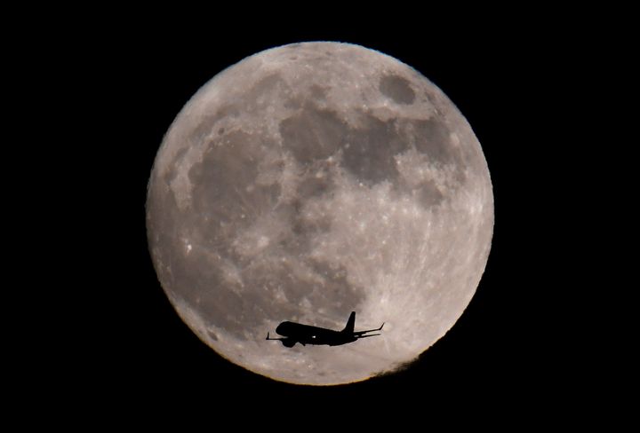 A passenger plane, with the moon seen behind, makes its final landing approach towards Heathrow Airport in London.