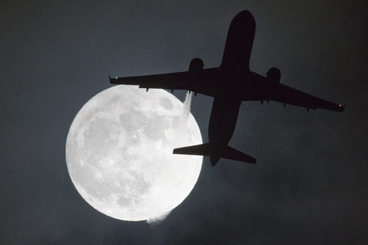 An airplane passes in front of the moon on its approach to London's Heathrow Airport.