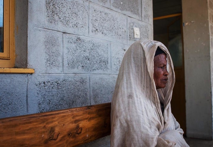 Bugune, wrapped in a shawl on a bench outside her local health clinic, is recovering from eyelid surgery that saved her sight