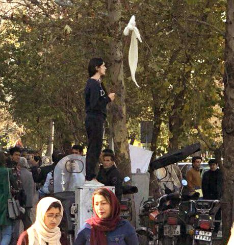 Iconic image of woman holding her hejab in the air, in defiance of laws, boldly attempting to declare a truce.