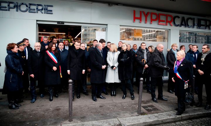 Paris Mayor Anne Hidalgo, in sash, French President Emmanuel Macron, to her right, French Interior Minister Gerard Collomb, beside Macron, and Macron's wife, Brigitte Macron, in white coat, join other officials in paying their respects at a memorial outside the Hyper Casher supermarket on Sunday.