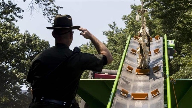 A New York State Environmental Conservation officer salutes as an ivory sculpture rolls into a crusher. The state is one of s