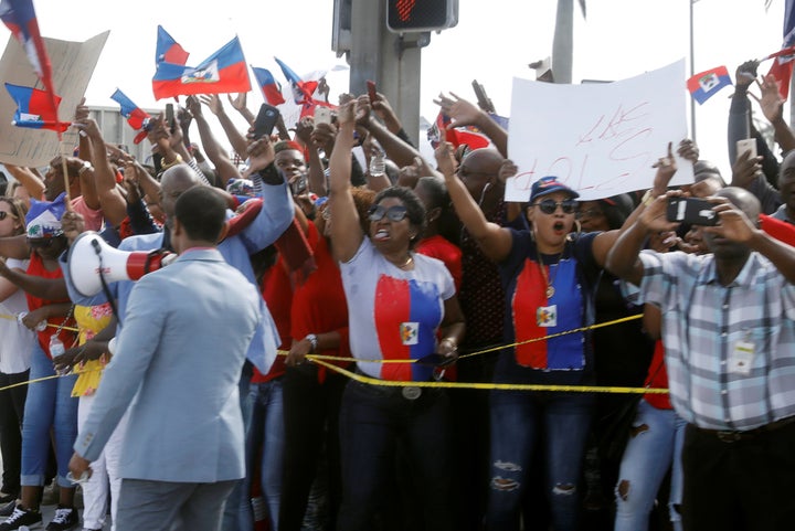 Demonstrators hold up Haitian flags and shout as President Donald Trump's motorcade passes in West Palm Beach, Florida, on Jan. 15, 2018.