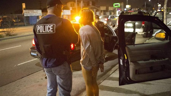 A 17-year-old girl in handcuffs is questioned by a vice squad policeman with the Los Angeles Police Department. Around the co