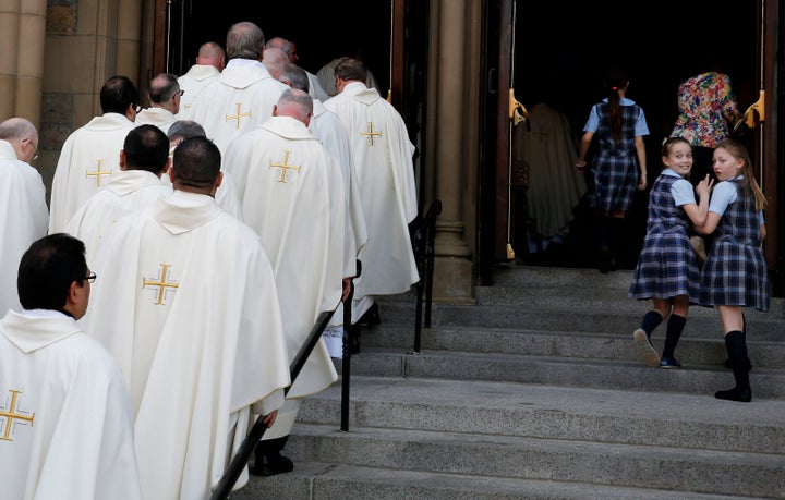 Two Catholic school girls look on as priests file into the Cathedral of the Holy Cross in Boston for Mass.