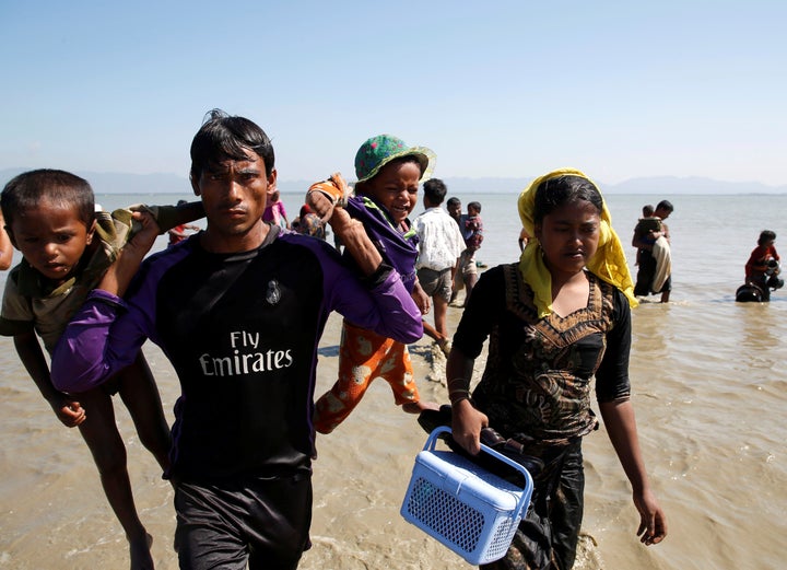 A Rohingya refugee man holding children walks towards the shore as they arrive on a makeshift boat after crossing the Bangladesh-Myanmar border, at Shah Porir Dwip near Cox's Bazar, Bangladesh, Nov. 9, 2017.