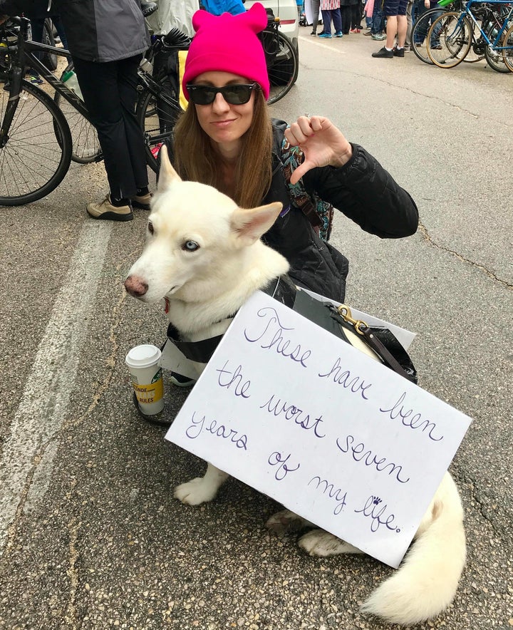 Stephanie Rzepka and her dog Hattie, wearing a sign reading "These have been the worst seven years of my life."