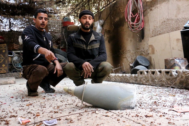 Syrian men sit next to an unexploded missile after an Assad regime air attack on the opposition in the besieged town of