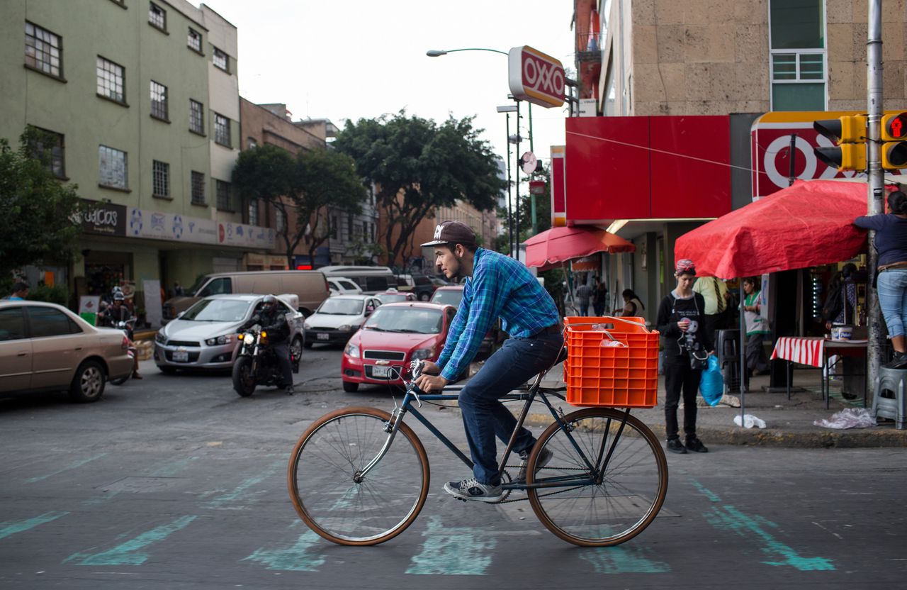 A man rides a bicycle past traffic in Mexico City. Investment in a public bicycle access program is one step the city has taken to combat air pollution.