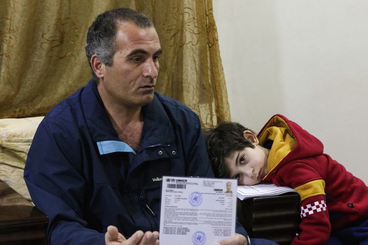 Faraj Ghazi al-Jamous, a Syrian refugee who was prevented from traveling to the U.S. because of the ban, sits in a living room with his son showing U.N. paperwork verifying his refugee status.